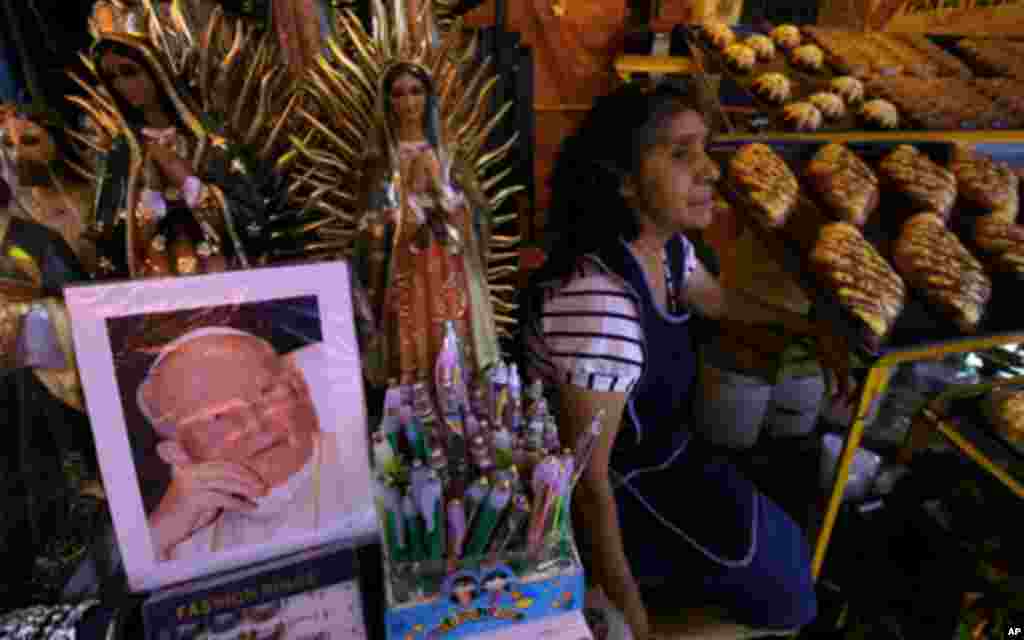 A woman selling bread sits next to a stand selling religious items, including a photo showing the late Pope John Paul II, at the Basilica of Guadalupe in Mexico City, April 28, 2011. Thousands of faithful are expected to begin arriving at the Basilica to 