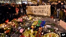 People hold a banner reading "I am Brussels" behind flowers and candles mourn for the terror attack victims at Place de la Bourse in the center of Brussels, March 22, 2016.