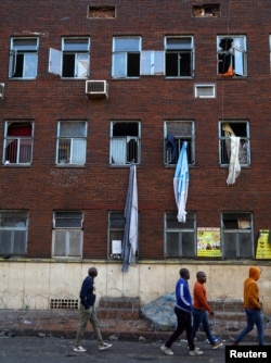 FILE - Men walk past sheets allegedly used by people to escape the scene of a deadly blaze at an apartment block in Johannesburg, South Africa September 1, 2023.