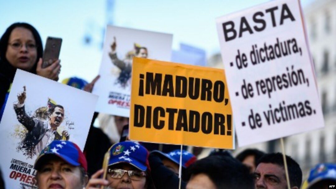 La gente sostiene pancartas que dicen "Maduro, dictador!" y "Basta de dictadura, represión y víctimas" durante una manifestación convocada por ciudadanos venezolanos contra el presidente Nicolás Maduro, en Madrid.