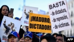 La gente sostiene pancartas que dicen "Maduro, dictador!" y "Basta de dictadura, represión y víctimas" durante una manifestación convocada por ciudadanos venezolanos contra el presidente Nicolás Maduro, en Madrid.