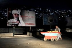 An Afghan street vendor pulls his hand cart in front of an election poster of Afghan President Ashraf Ghani, in Kabul, Afghanistan, Sept. 9, 2019. President Donald Trump's sudden halt to U.S.-Taliban talks looks like a gift to the Afghan president.