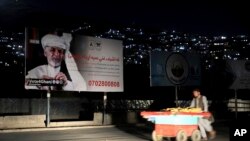 In this Sept. 9, 2019, photo, an Afghan street vendor pulls his hand cart in front of an election poster of Afghan President Ashraf Ghani, who seeks a second term, in Kabul, Afghanistan.