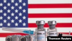 Vials labelled "COVID-19 Coronavirus Vaccine" and sryinge are seen in front of displayed USA flag in this illustration