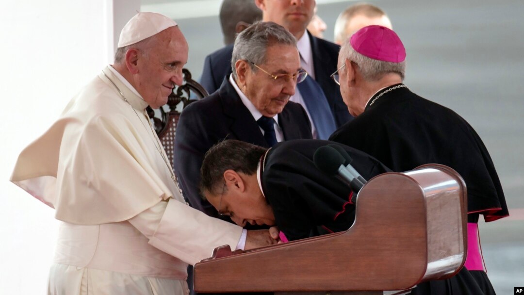 A member of Cuba's church leadership kisses the hand of Pope Francis as Cuban President Raul Castro stands alongside during the pope's arrival ceremony at the airport in Havana, Sept. 19, 2015.