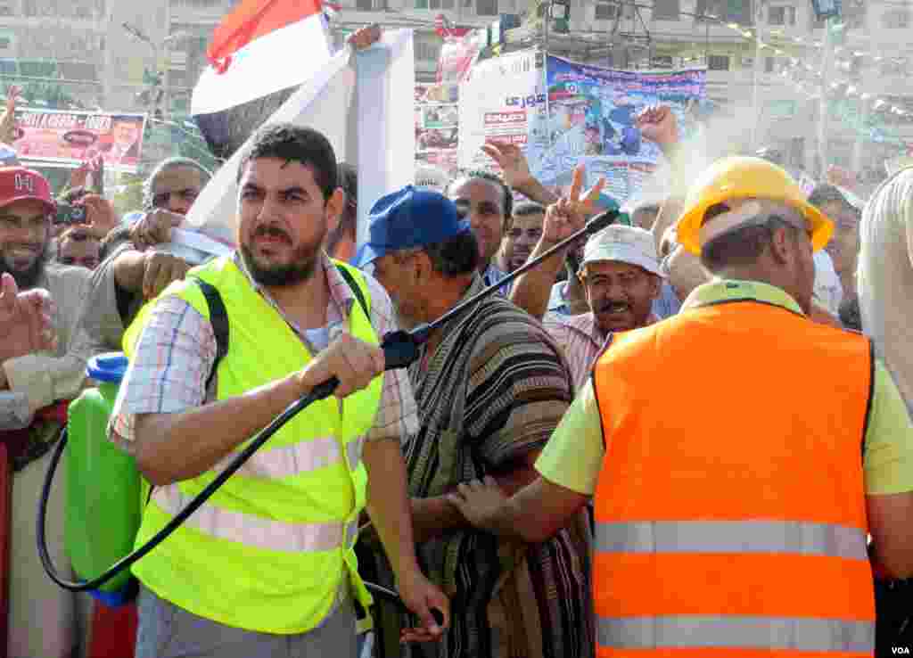 Men spray the hot crowds with cold water from plastic water packs and bottles. Currently fasting for the holy month of Ramadan, no one in this crowd takes a drink. (Heather Murdock for VOA)