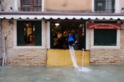 FILE - A man removes water from the flooded shop during a period of seasonal high water in Venice, Italy, Nov. 15, 2019.