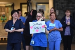 An NHS staff member wipes her eyes as she holds a sign to thank British veteran Captain Tom Moore, who raised money for the health care workers battling COVID-19, at Aintree University Hospital in Liverpool, north-west England, April 16, 2020.