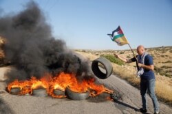 A Palestinian demonstrator throws a tire to a burning barricade, following a flare-up of Israeli-Palestinian violence, on a road near Tubas in the Israeli-occupied West Bank, May 15, 2021.