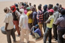 FILE - Migrants wait for trucks arriving from Algeria to unload their cargo, in order to earn money to pay for the trip north, at a giant desert trading post called "The Dune" in the no-man's land separating Niger and Algeria, June 3, 2018.