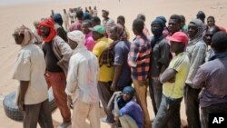 FILE - Migrants wait for trucks to unload their cargo at a giant desert trading post called "The Dune" in the no-man's land north of Assamaka, separating Niger and Algeria. taken June 3, 2018.