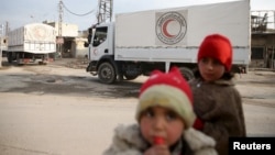 Children stand along a street as an aid convoy of Syrian Arab Red Crescent and United Nation (UN) drives through the rebel held besieged city of Douma towards the besieged town of Kafr Batna to deliver aid, on the outskirts of Damascus, Syria, Feb. 23, 2