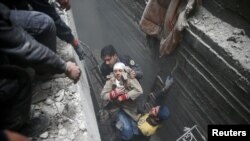 La défense civile syrienne aide une femme dans la ville assiégée de Douma, dans l'est de la Ghouta, à Damas, en Syrie, le 22 février 2018.