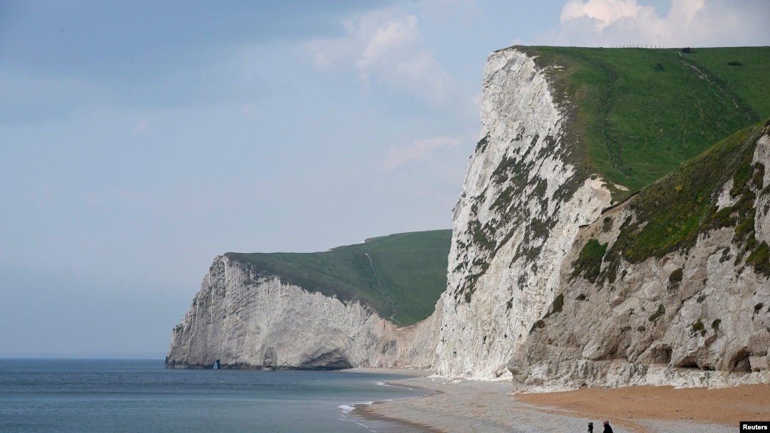 FILE - A man takes photographs pointing south on the beach at Durdle Door with the English Channel sea connecting Britain to mainland Europe seen behind, in south west England, May 13, 2016. 