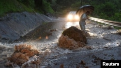 FILE - In early July, flooding struck southwestern Japan, including Hita, in Oita Prefecture, where a flooded road with fallen rocks is pictured, July 5, 2017. In northeast Japan, tens of thousands have been told to evacuate because of heavy rain and flooding.