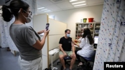 A woman takes a picture of a man as he receives a third shot of the COVID-19 vaccine as the country launches booster shots for people over 40 years old, in Jerusalem, August 20, 2021. 