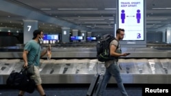 Travelers pass a sign alerting them to distance at LaGuardia Airport, during the outbreak of the coronavirus disease (COVID-19), in New York, June 29, 2020. 