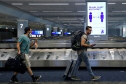 Travelers pass a sign alerting them to distance at LaGuardia Airport, during the outbreak of the coronavirus disease (COVID-19), in New York, June 29, 2020.