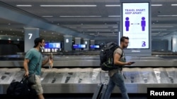 Travelers pass a sign alerting them to distance at LaGuardia Airport, during the outbreak of the coronavirus disease (COVID-19), in New York, June 29, 2020. 