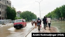 Les piétons marchent sur un trottoir boueux tandis que les véhicules pataugent dans une rue inondée par des pluies diluviennes à N'Djamena, au Tchad, le 19 août 2020. (Photo: André Kodmadjingar/VOA)