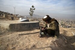 FILE - A man reads the Quran besides his relative's grave in a cemetery on the outskirts of Kabul, Afghanistan, Jan. 14, 2021.