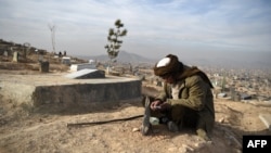 FILE - A man reads the Quran besides his relative's grave in a cemetery on the outskirts of Kabul, Afghanistan, Jan. 14, 2021.