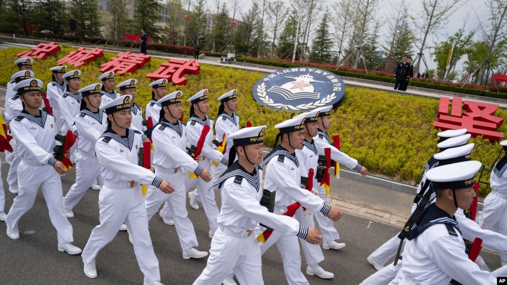 水兵们列队走过山东省青岛市中国人民解放军海军潜艇学院的徽章。(2024年4月21日)