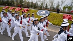 水兵们列队走过山东省青岛市中国人民解放军海军潜艇学院的徽章。(2024年4月21日)
