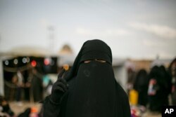 FILE - A woman poses at Al-Hol camp, March 31, 2019, which holds families of Islamic State members, near Hasakeh, Syria.