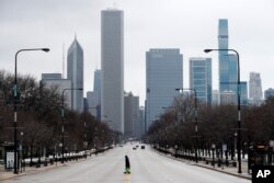 An elderly lady walks across the usually busy Columbus Drive that splits Chicago's Grant Park in half, on the first work day since Illinois Gov. J.B. Pritzker gave a shelter in place order last week, March 23, 2020.