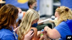 FILE - Harper Stukus, 8, center, receives a COVID-19 vaccine from a registered nurse, right, as a certified child life specialist helps with distraction during a COVID-19 vaccine clinic at Nationwide Children's Hospital in Columbus, Ohio, Nov. 3, 2021.
