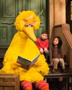 FILE - Big Bird, voiced by Caroll Spinney, reads to children during a taping of Sesame Street in New York, April 10, 2008.