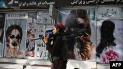 Një luftëtar taleban duke ecur në Kabul përpara një salloni bukurie në dritaret e të cilit ka filluar mbulimi me bojë i imazheve të grave
