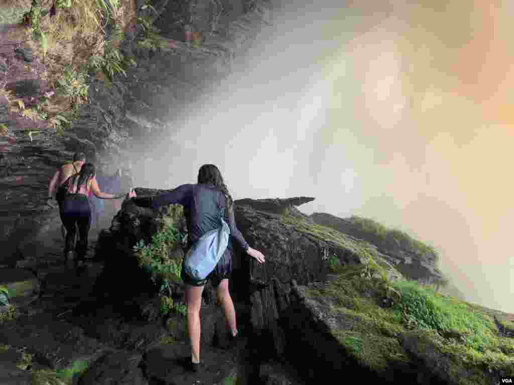 Turistas exploran una cueva detrás de la cascada Hacha en Canaima, Venezuela