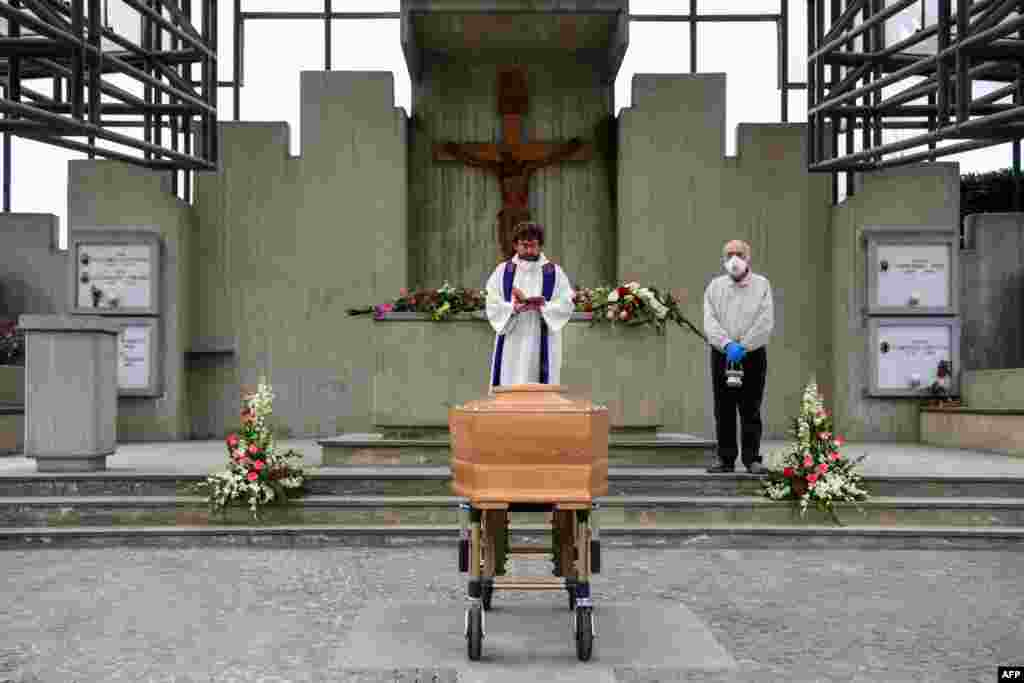 A priest (C) reads prayers from the book of funeral rites by the coffin of a deceased person in the cemetery of Grassobbio, Lombardy, in the absence of quarantined relatives.