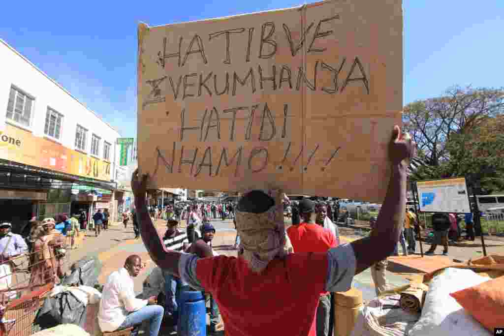 Vendors hold placards written in the local language, shona, saying they will not move after they were removed from the streets of Harare, Wednesday, July, 8, 2015. Minor scuffles ensued as police officers drove out thousands of vendors selling their wares on the sidewalks and pavements of Harare. 