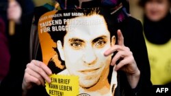 FILE - An Amnesty International activist holds a picture of Saudi blogger Raif Badawi during a protest against his flogging punishment, in front of Saudi Arabia's embassy in Berlin, Germany, Jan. 29, 2015.