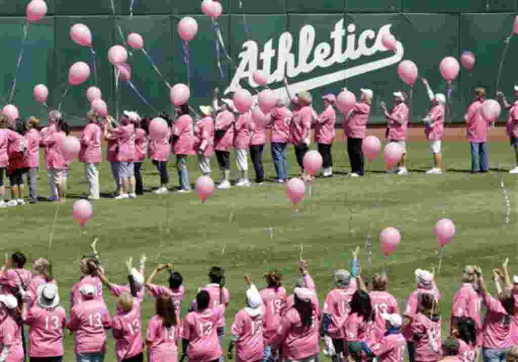 Durante un partido de béisbol en Oakland, sobrevivientes de cáncer de mama saludan a los aficionados del los equipos Marineros de Seattle y los Atletas de Oakland.