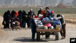 FILE - Iraqi civilians walk toward Iraqi security forces after fleeing their homes due to fighting between government forces and Islamic State militants, on the western side of Mosul, Iraq, March 9, 2017.