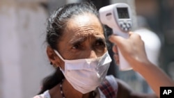 Una mujer mira a un trabajador de la salud mientras mide su temperatura como medida de precaución contra la propagación del coronavirus, antes de que se le permita ingresar a un comedor de beneficencia en Caracas, Venezuela.