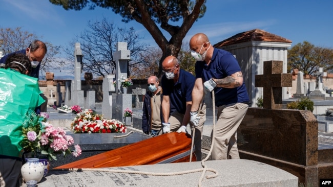 TOPSHOT - Mortuary employees wearing face masks burry the coffin of a COVID-19 coronavirus victim at Fuencarral cemetery in Madrid on March 29, 2020. - Spain confirmed another 838 deaths in 24 hours from coronavirus , a new daily record bringing the…