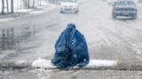 An Afghan burqa-clad woman looks for alms along a street, during the first heavy snowfall this winter in Kabul, Jan. 2, 2025. 