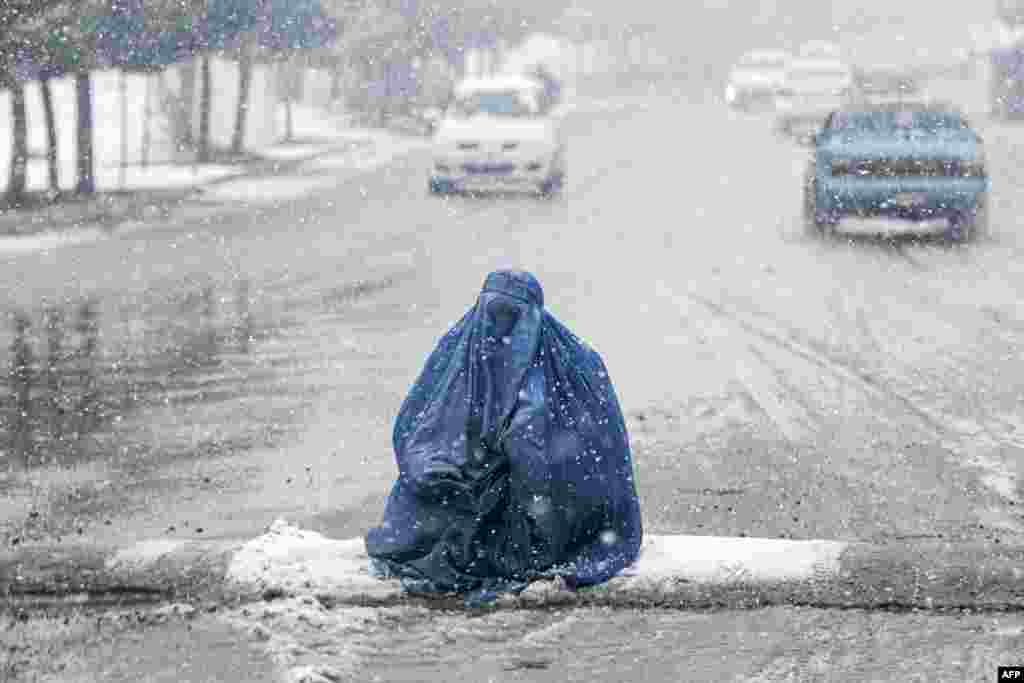 An Afghan burqa-clad woman asks for alms along a street, during the first heavy snowfall this winter in Kabul.