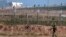 FILE - A Turkish soldier walks by the border fence with Syria while in the background, Kurdish fighters, top right, advance, as civilians, top left, flee the outskirts of Tal Abyad, Syria. 