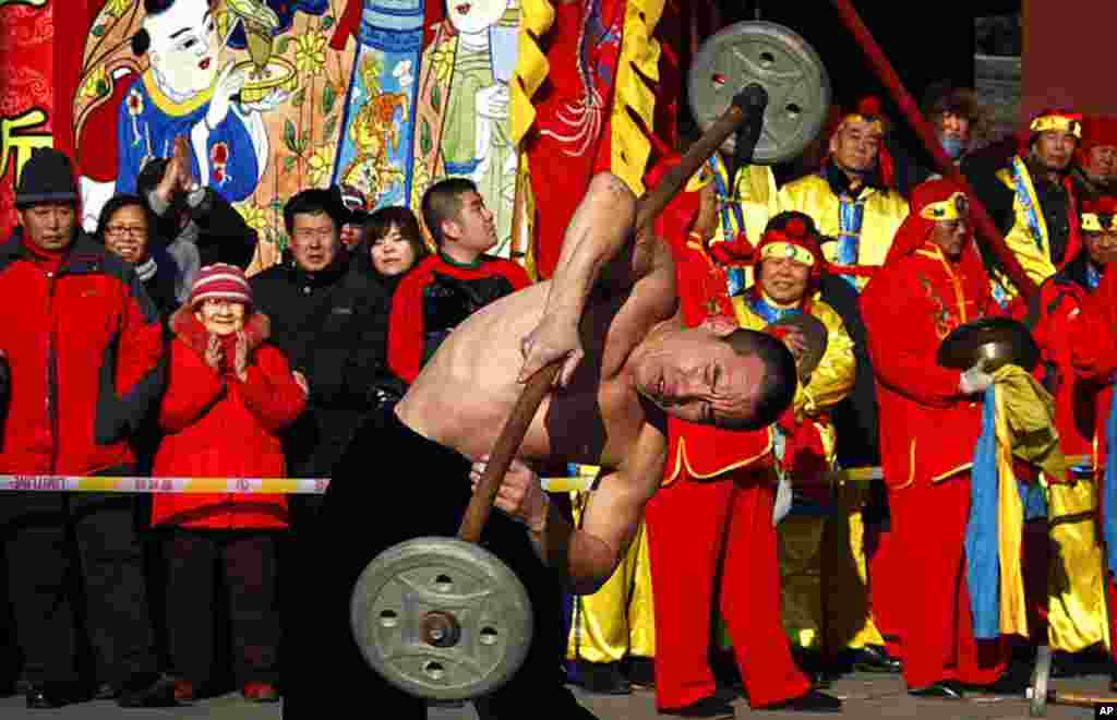 A performer known as a "strong man" twirls weights on his shoulder as he performs in front of a crowd during Chinese new year celebrations at the 700-year-old Dongyue Temple in Beijing. The temple is the largest of its kind in northern China for the Zheng