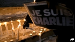 A woman holding a sign that read in French "I am Charlie" lights a candle during a demonstration in solidarity with those killed in an attack at the Paris offices of the weekly newspaper Charlie Hebdo in Kosovo capital Pristina, Wednesday, Jan. 7, 2015. 