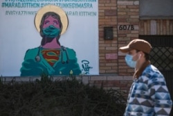 A man wearing a face mask to protect against coronavirus walks past a graffiti with the inscription reading "stay at home and let's take care of each other" in Erd, just south of Budapest, April 10, 2020.