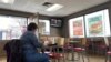 A woman eats in a fast food restaurant as a television shows live coverage of U.S. President Donald Trump's U.S. Senate impeachment trial three days before the Iowa caucus in Des Moines, Iowa, Jan. 31, 2020.
