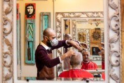 A barber wears a mask to help prevent the spread of the coronavirus as he cuts a customer's hair at his salon, in Beirut, Lebanon, May 4, 2020.