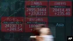 A woman wearing a face mask walks past an electronic stock board showing Japan's Nikkei 225 and other Asian countries' index at a securities firm in Tokyo, May 11, 2020. 